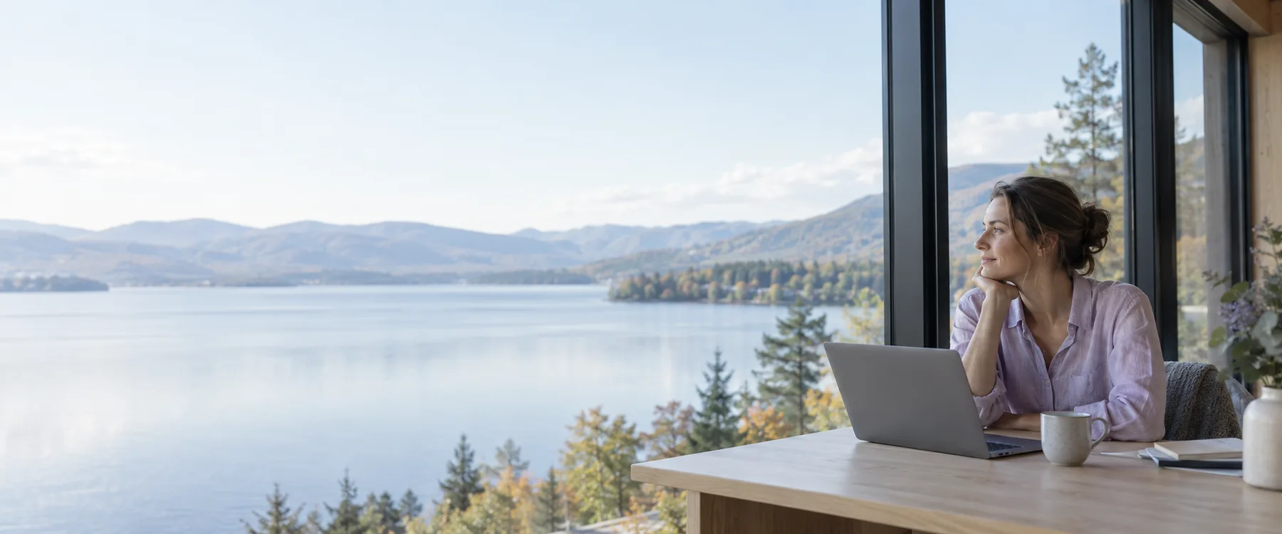 A woman takes a quiet moment by a lake, with her laptop nearby.
